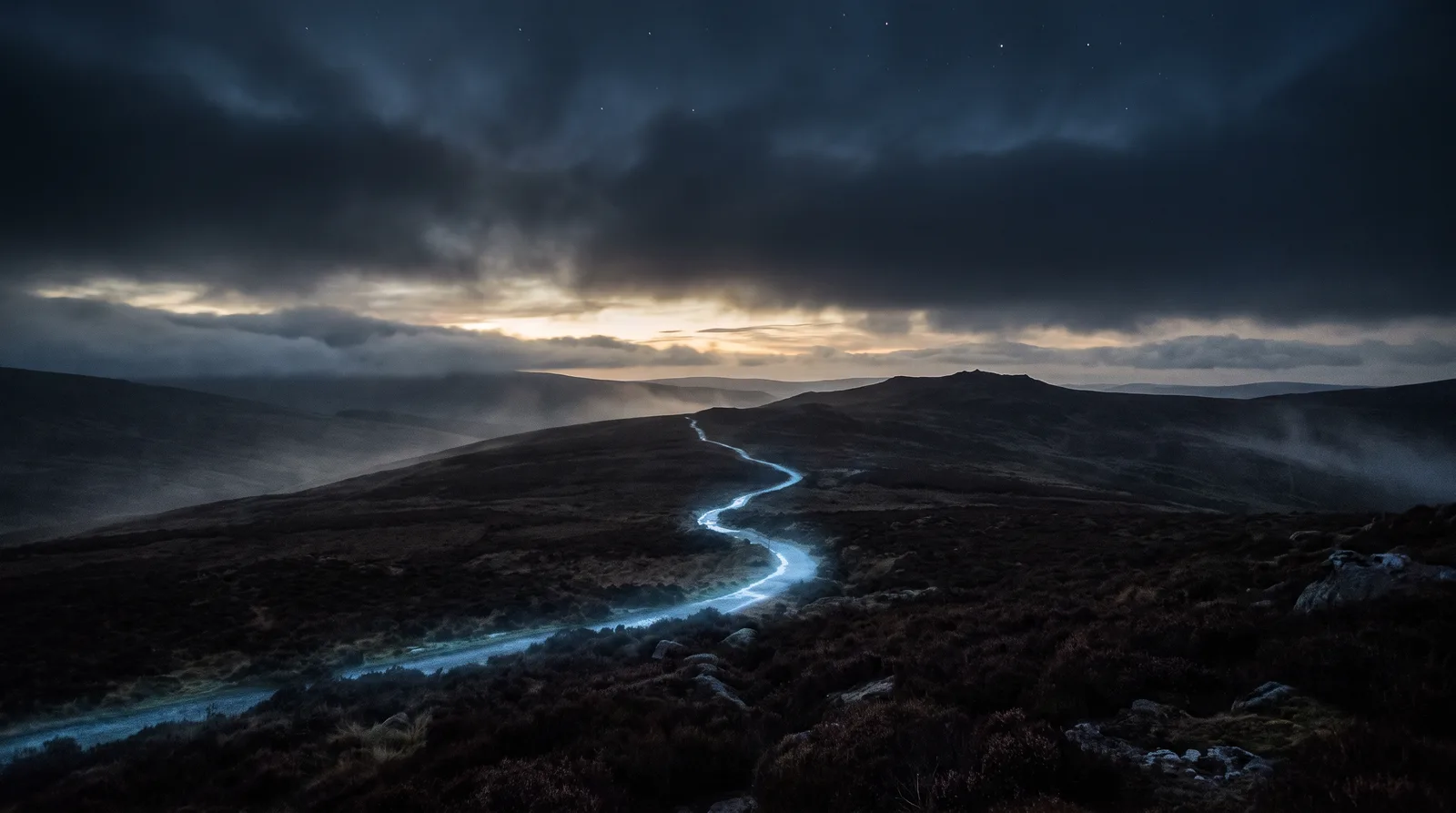 Caminho de luz azul cruzando colinas escuras em direção ao amanhecer